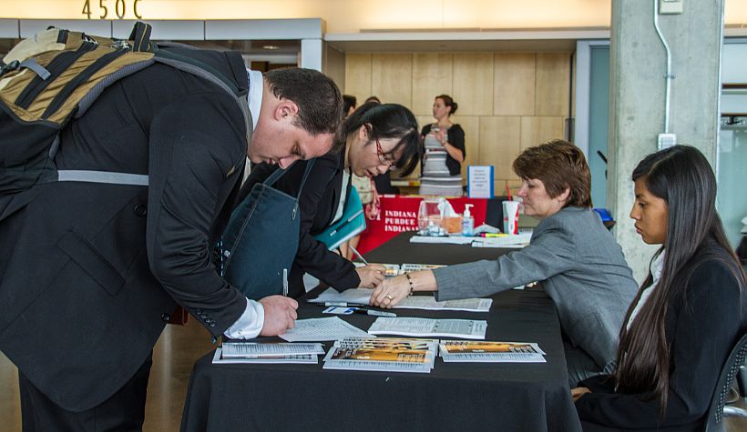 Students in business suits sign in at a table during a campus career fair.