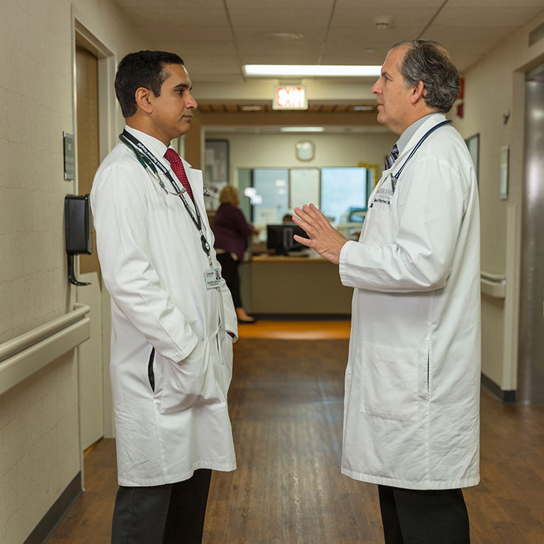 Two physicians in white lab coats have a conversation in a hospital hallway.