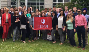 Kelley students studying human resources abroad in Germany stand together, holding an IUPUI flag.